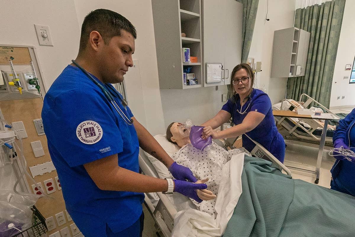 Two San Juan nursing students demonstrate checking a pulse and providing oxygen on a dummy