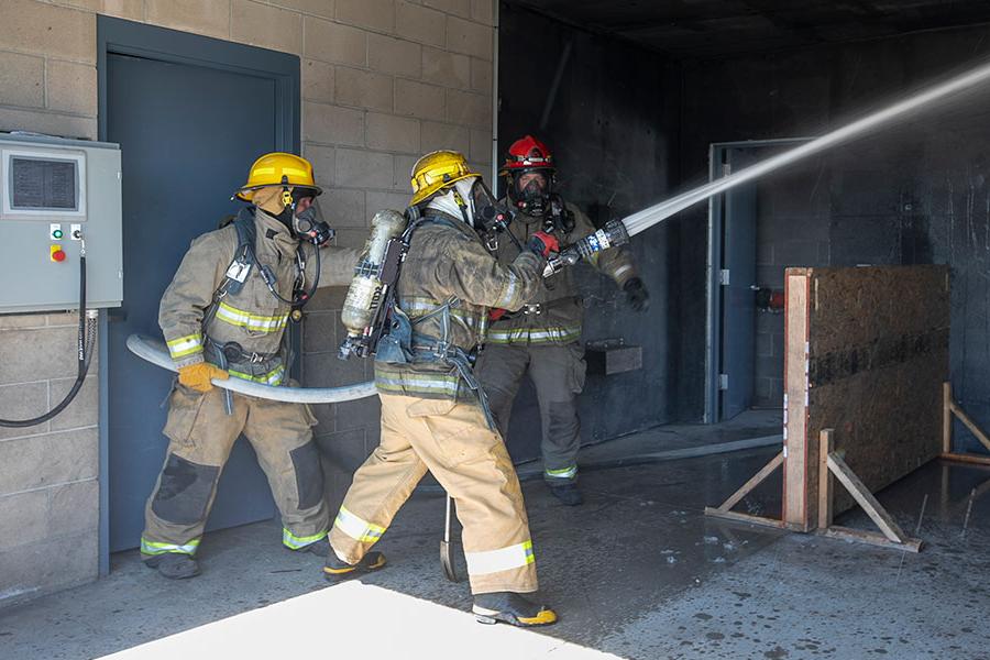Three students with firefighter equipment spraying out fire