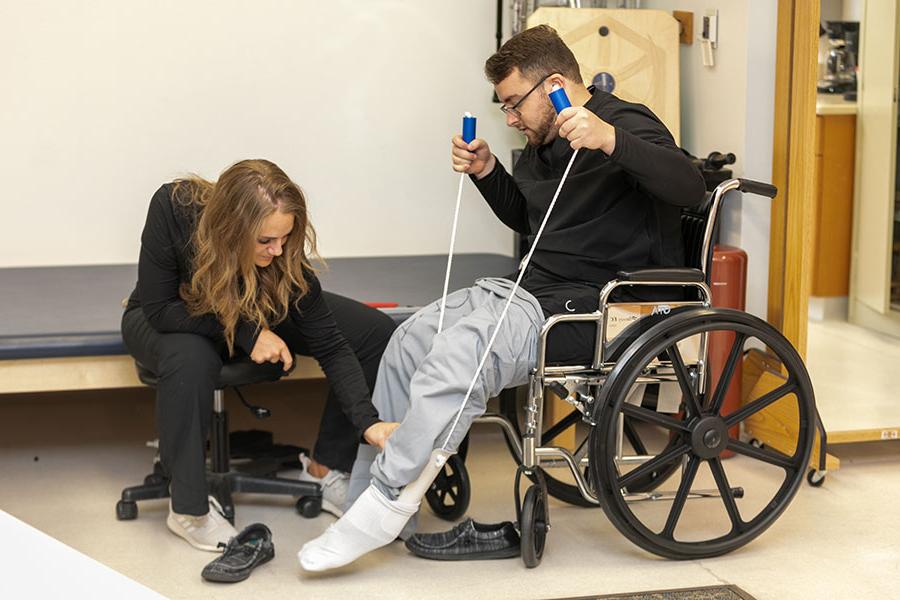 A student assesses the leg of another student who is sitting in a wheelchair